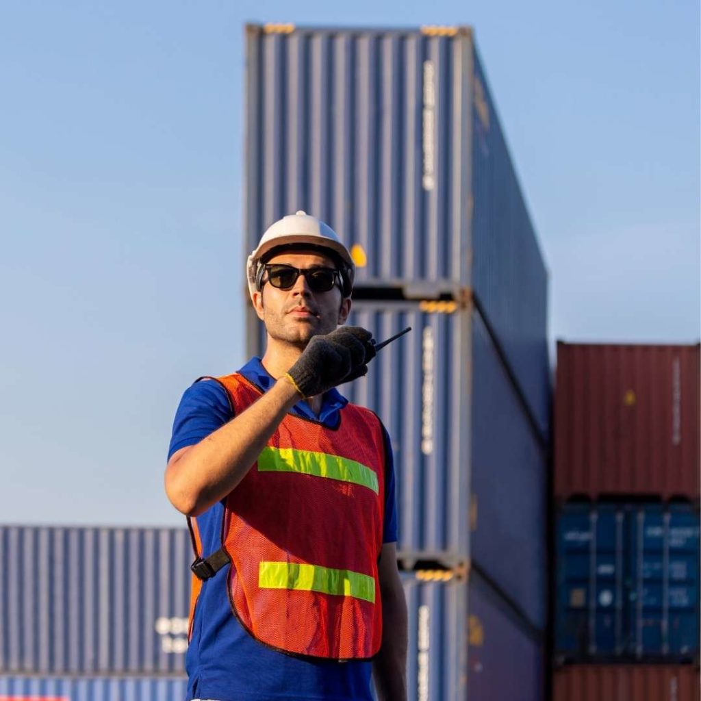 Man in construction vest using walkie talkie in shipping yard