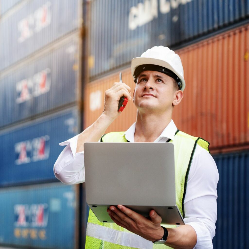 man in front of shipping containers with radio and laptop