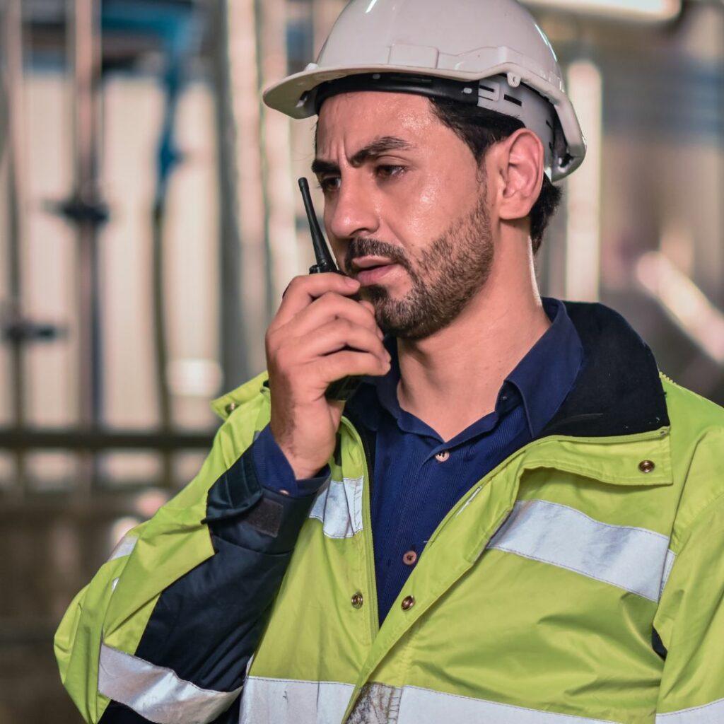 man in hard hat talking into radio, looking concerned